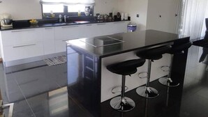 A modern kitchen with white cabinets, a black countertop, and a central island with bar stools. - Casa do Penedo Gordo (Fafe)