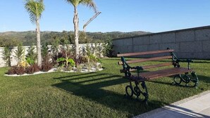 A park with a bench, palm trees, and a stone wall. - Casa do Penedo Gordo (Fafe)