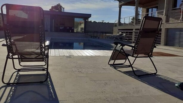 An outdoor pool area with two lounge chairs and a modern building in the background. - Casa do Penedo Gordo (Fafe)