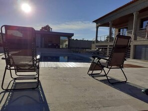 An outdoor pool area with two lounge chairs and a modern building in the background. - Casa do Penedo Gordo (Fafe)