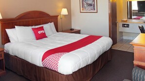 Hotelkamer met een groot bed, een houten hoofdbord, een nachtkastje met lamp, een ingelijst schilderij aan de muur, en een badkamer zichtbaar door een open deur.