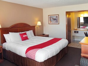 Hotelkamer met een groot bed, een houten hoofdbord, een nachtkastje met lamp, een ingelijst schilderij aan de muur, en een badkamer zichtbaar door een open deur.