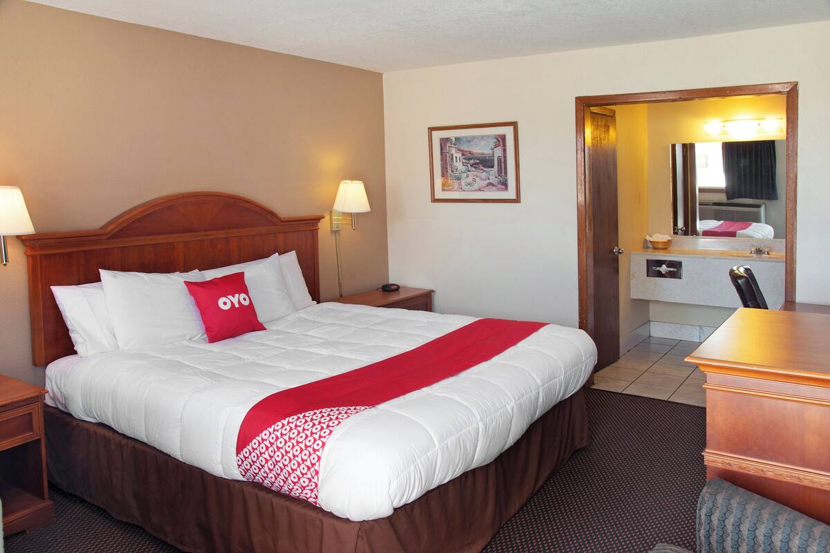 Une chambre d’hôtel avec un grand lit, deux tables de chevet, un bureau, une chaise, un miroir et un tableau encadré au mur.