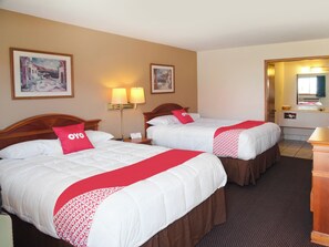 Hotelkamer met twee bedden, elk voorzien van witte beddengoed en rode accenten, een nachtkastje met een lamp, en een zichtbare badkamer door een open deur.