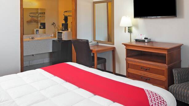 Ett hotellrum med en säng, ett skrivbord, en stol, en tv och en spegel.