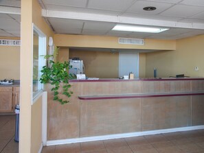 Un espace d’accueil comprenant un comptoir, un réfrigérateur, une plante et une fenêtre.