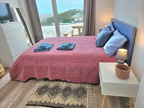 A bedroom with a large bed, a nightstand, a lamp, and a view of the outdoors. - Ericeira Ribamar Sea View Villa (Mafra)