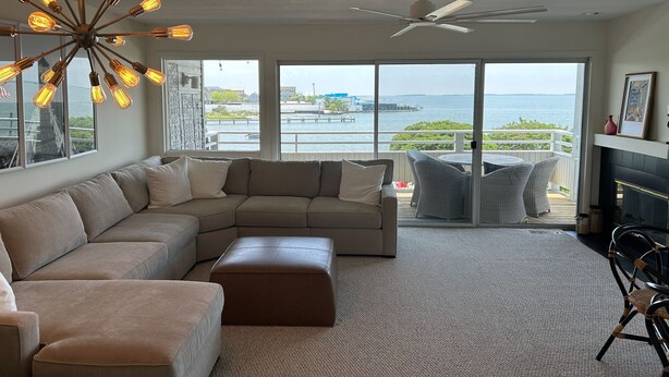 A modern living room with a sectional sofa, a ceiling fan, and a view of the ocean.