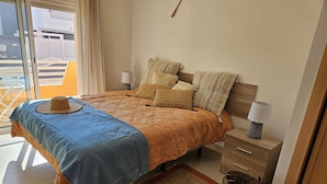 A bedroom with a bed, bedside tables, a nightstand, a window, and a view of the outside. - Balcony Pool Royal Cabanas Golf 18 (Tavira)