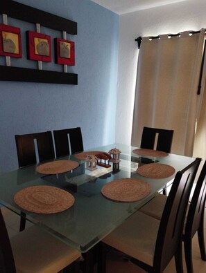 A dining area with a glass table, brown woven placemats, and dark wooden chairs.