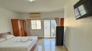 A hotel room with a bed, a wardrobe, a television, and a sliding glass door leading to an outdoor area. - Malee Guesthouse & Restaurant (Pattaya)