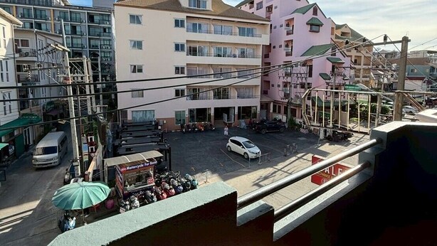 A multi-story building with balconies, a parking lot, and a street view. - Malee Guesthouse & Restaurant (Pattaya)