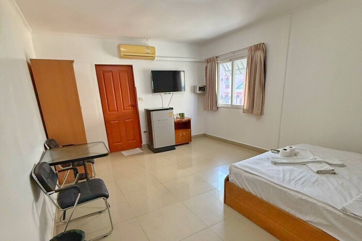 Una habitación de hotel con cama, escritorio y sillas, televisor y ventana con cortinas.
