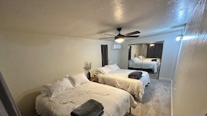 Ett hotellrum med två sängar, en takfläkt, ett litet bord med en vas och en spegel som reflekterar rummet.