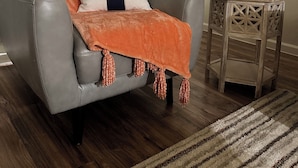 En grå lädersoffa med en orange pläd och en vit kudde med en blå rand. Ett litet träbord med en krukväxt står till höger.
