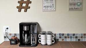 Ett kök med en kaffebryggare, fyra kaffemuggar, en hashtag och två väggskyltar.