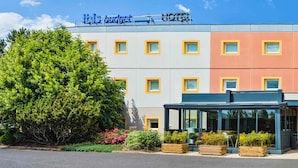 Een hotel met een moderne gevel, met een combinatie van wit en oranje, en een grote boom ervoor.