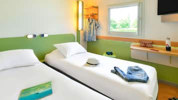 Habitación de hotel con dos camas, una ventana con vistas, un televisor montado en la pared y una mesita de noche con una botella de agua y un sombrero.