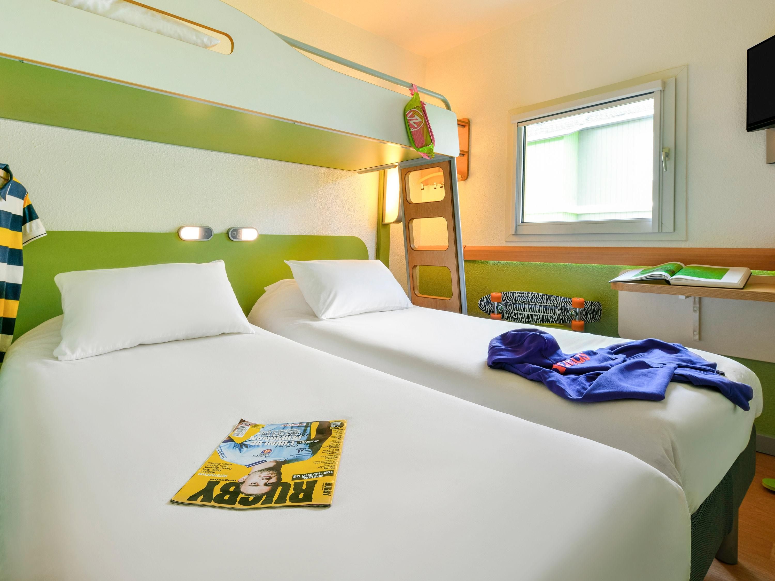 A hotel room with two beds, a window, a desk, and a ladder.