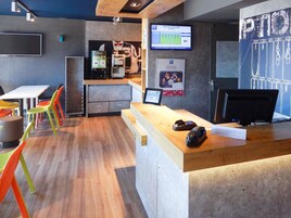 Una moderna zona de recepción con un mostrador de madera, una pantalla digital mostrando un mensaje de bienvenida y sillas coloridas.