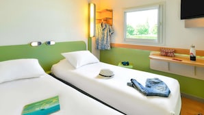 Een hotelkamer met twee eenpersoonsbedden, een nachtkastje, een televisie en een raam met uitzicht op groen.
