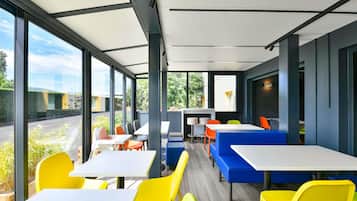 Un espace de restauration intérieur moderne, doté de grandes fenêtres, de sièges aux couleurs vives, jaune et bleu, et offrant une vue sur la verdure environnante.
