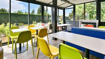 Un comedor moderno con amplios ventanales, sillas amarillas y verdes, y una mesa blanca.