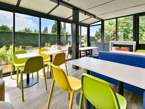 Un espace repas moderne avec de grandes fenêtres, des chaises jaunes et vertes, et une table blanche.