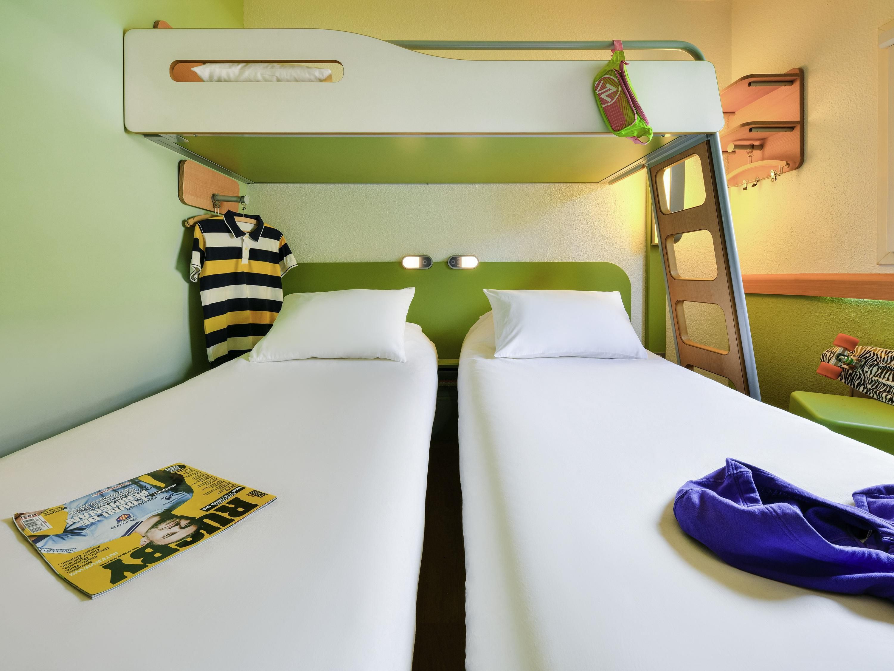 A bunk bed room with two single beds, a striped shirt hanging on the wall, and a magazine on one bed.