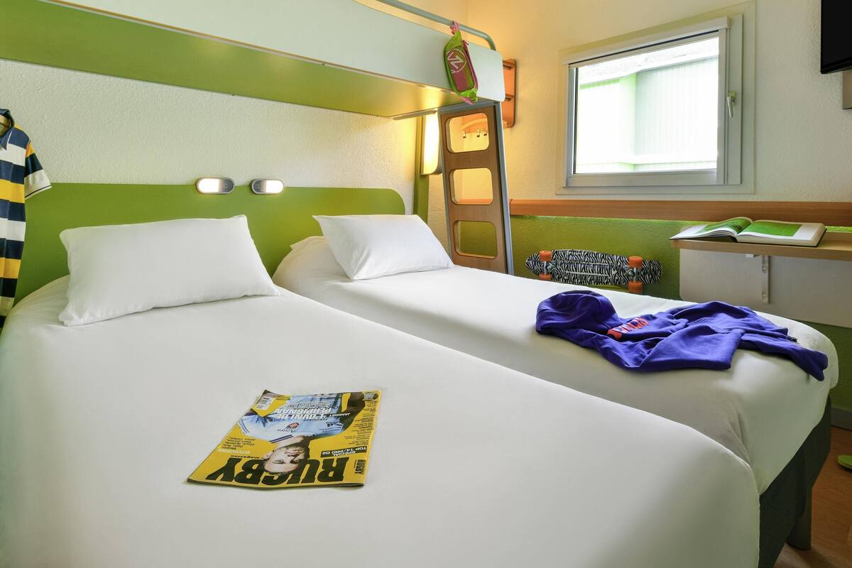 Habitación de hotel con dos camas, una escalera, un ventanal y una revista sobre una cama.
