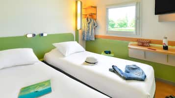 A hotel room with two single beds, a bedside table, a TV, and a window with a view of greenery.