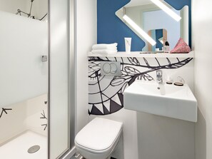 Une salle de bain moderne avec des toilettes blanches, un lavabo surmonté d’un miroir et un espace douche.