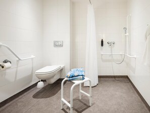 Et moderne badeværelse med hvide fliser, toilet, brusebad med glasdør og en hvid bænk.