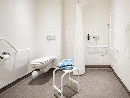 Un baño moderno con azulejos blancos, un inodoro, una ducha con puerta de vidrio y un banco blanco.
