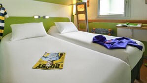 Une chambre d’hôtel avec deux lits, une échelle, une fenêtre et un magazine posé sur l’un des lits.
