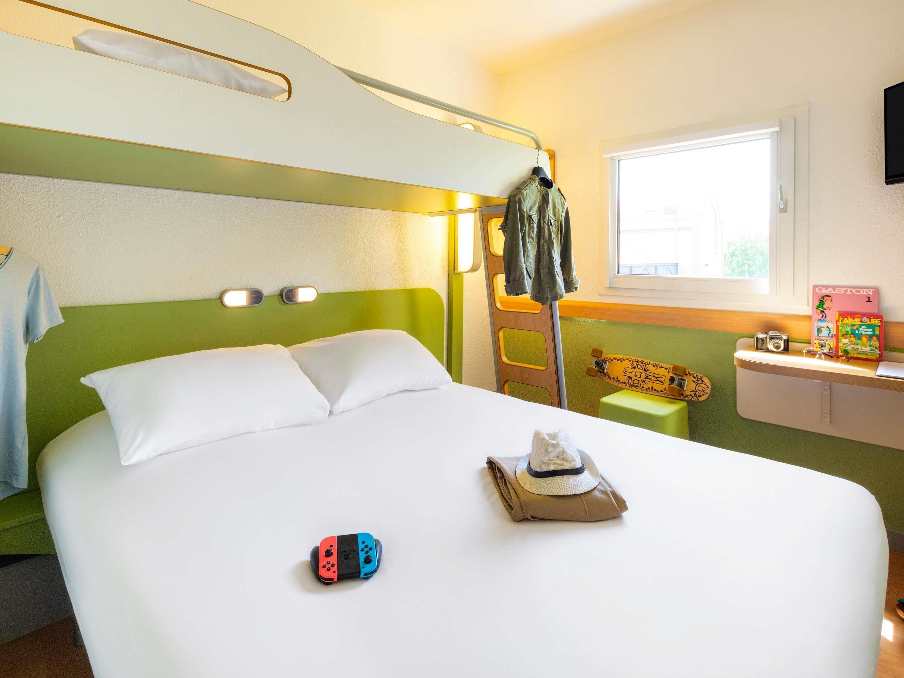A hotel room with a bunk bed, a small desk with a computer, a window, and a skateboard.