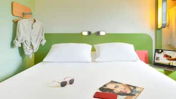 Una habitación de hotel con cabecera verde, dos almohadas blancas, una cama con sábana blanca, un par de gafas de sol, un teléfono inteligente rojo y una revista sobre la mesita de noche.