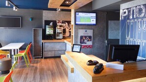 Een moderne receptiebalie met een houten toonbank, een scherm met een welkomstboodschap en kleurrijke stoelen.
