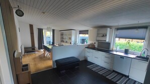 Una cocina moderna con baldosas oscuras, armarios blancos y encimera negra. Cuenta con una zona de comedor con mesa y sillas, y un pequeño banco.