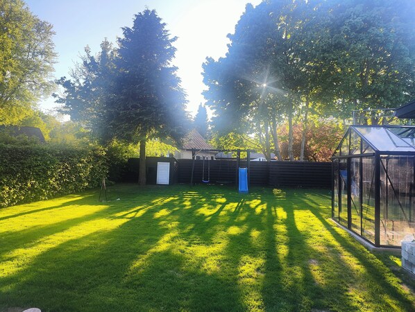 Ein gepflegter Garten mit Rasen, einer blauen Rutsche und einem Glashaus.