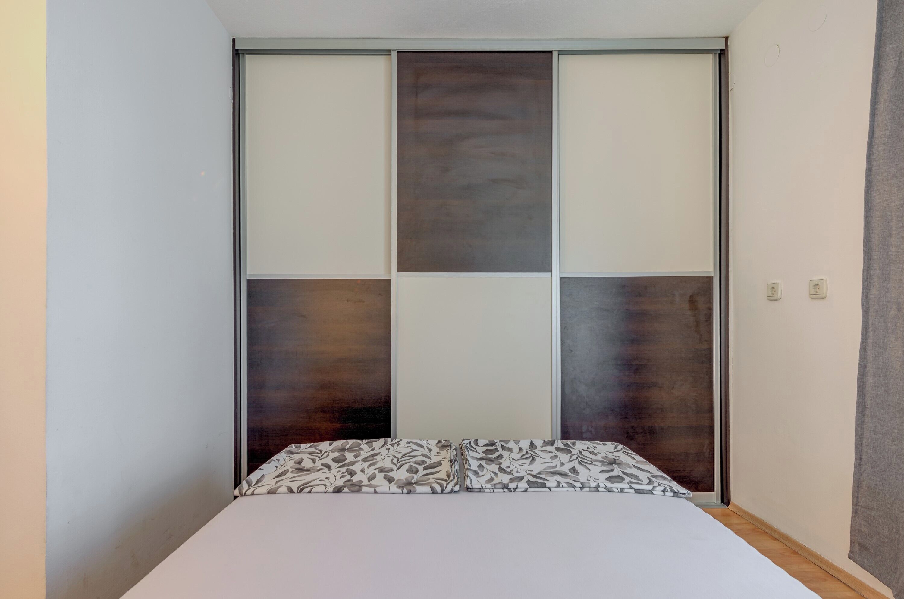 Ein Schlafzimmer mit einem Bett, einer Schiebetür mit dunklem Paneel und einer hellen Wand.