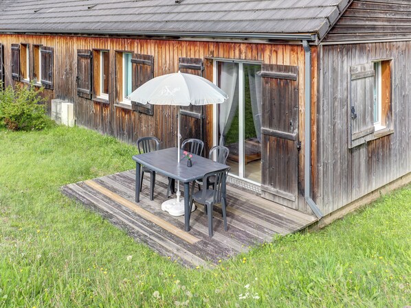 A rustic wooden building with a patio area featuring a table and chairs, a white umbrella, and a sliding glass door.