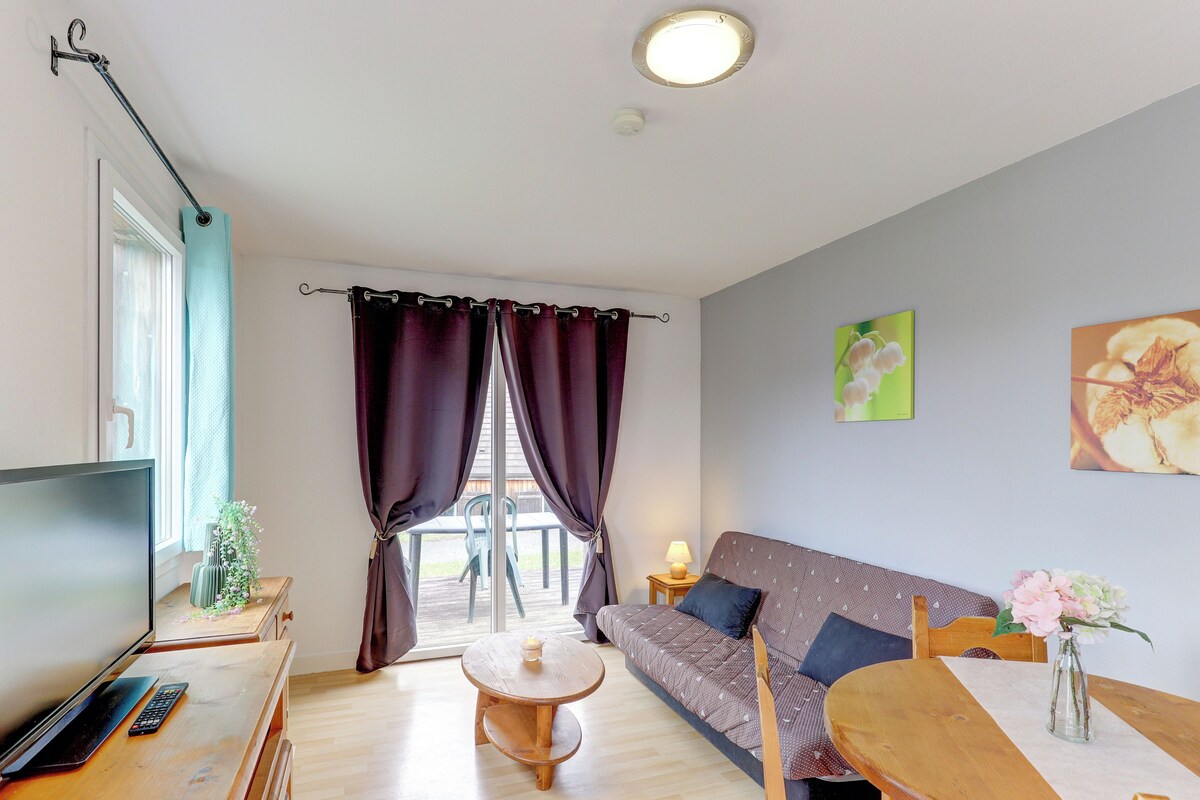 Una sala de estar con un sofá, televisor, mesa y ventana con cortinas.