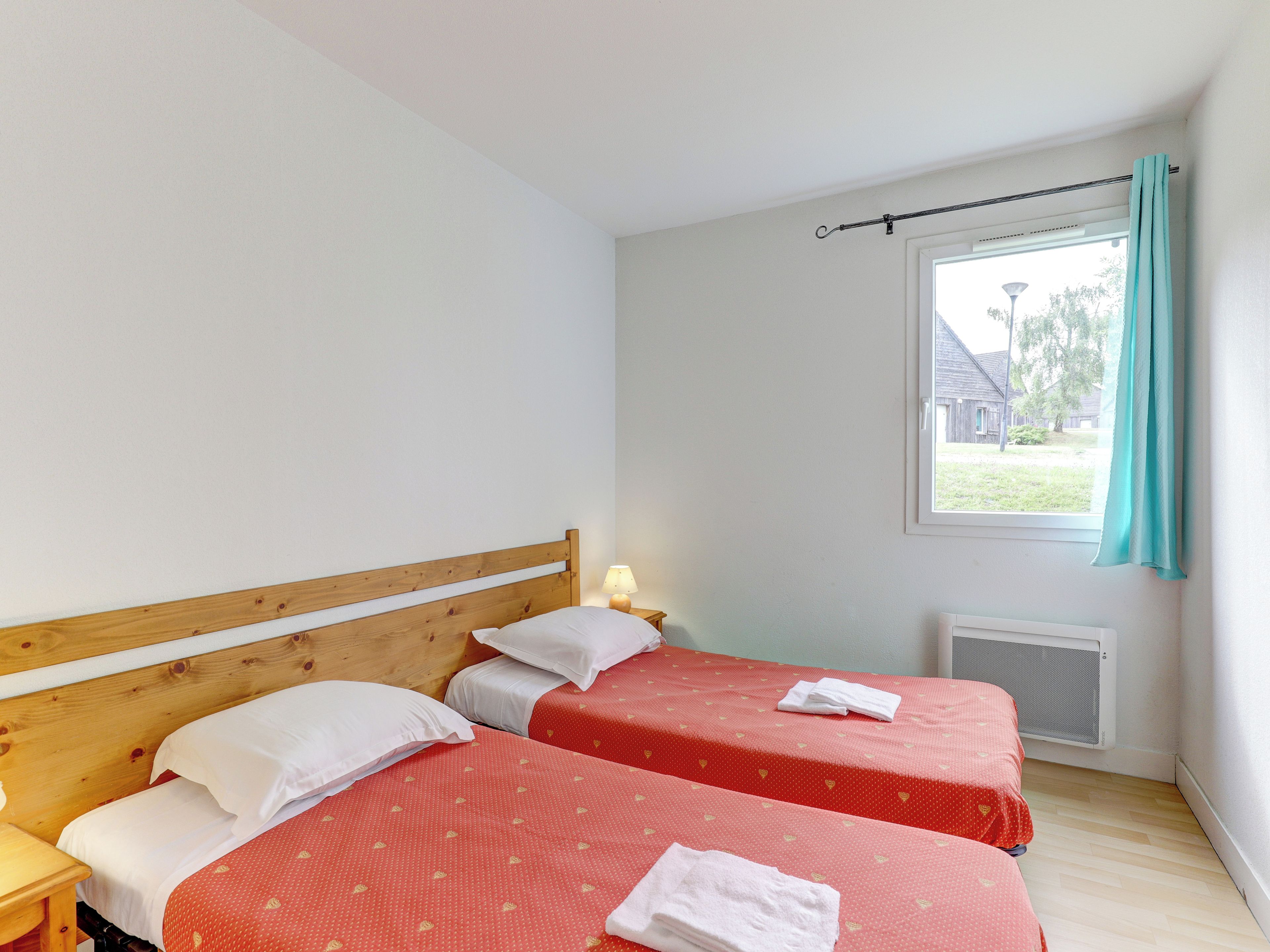A bedroom with two beds, a wooden headboard, a nightstand, a lamp, and a window with a curtain.