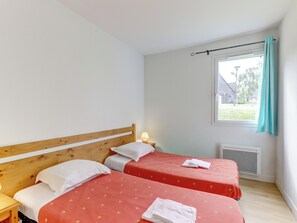 A bedroom with two beds, a wooden headboard, a nightstand, a lamp, and a window with a curtain. - Residence Le Domaine Du Bosquet (Miremont)