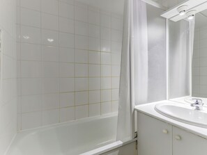 A bathroom with white tiled walls, a bathtub, a sink with a mirror, and a shower curtain. - Residence Le Domaine Du Bosquet (Miremont)