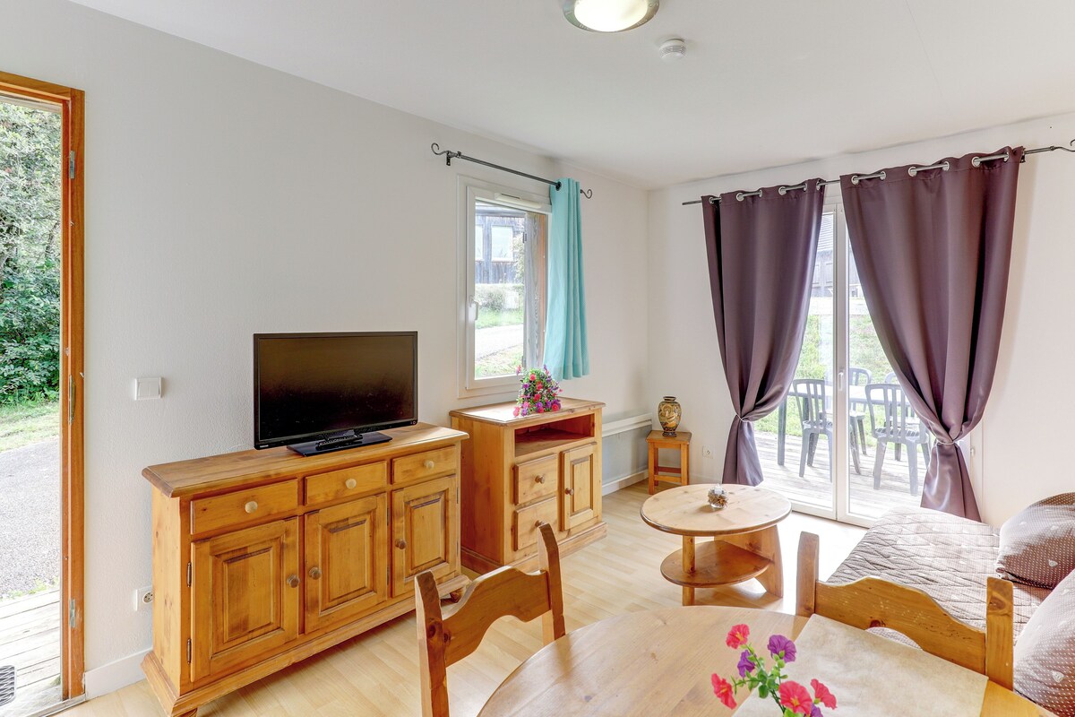 A room with a TV, wooden furniture, a small table, and a window with curtains.