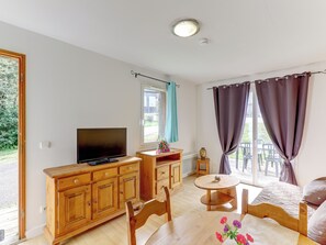 A room with a TV, wooden furniture, a small table, and a window with curtains.