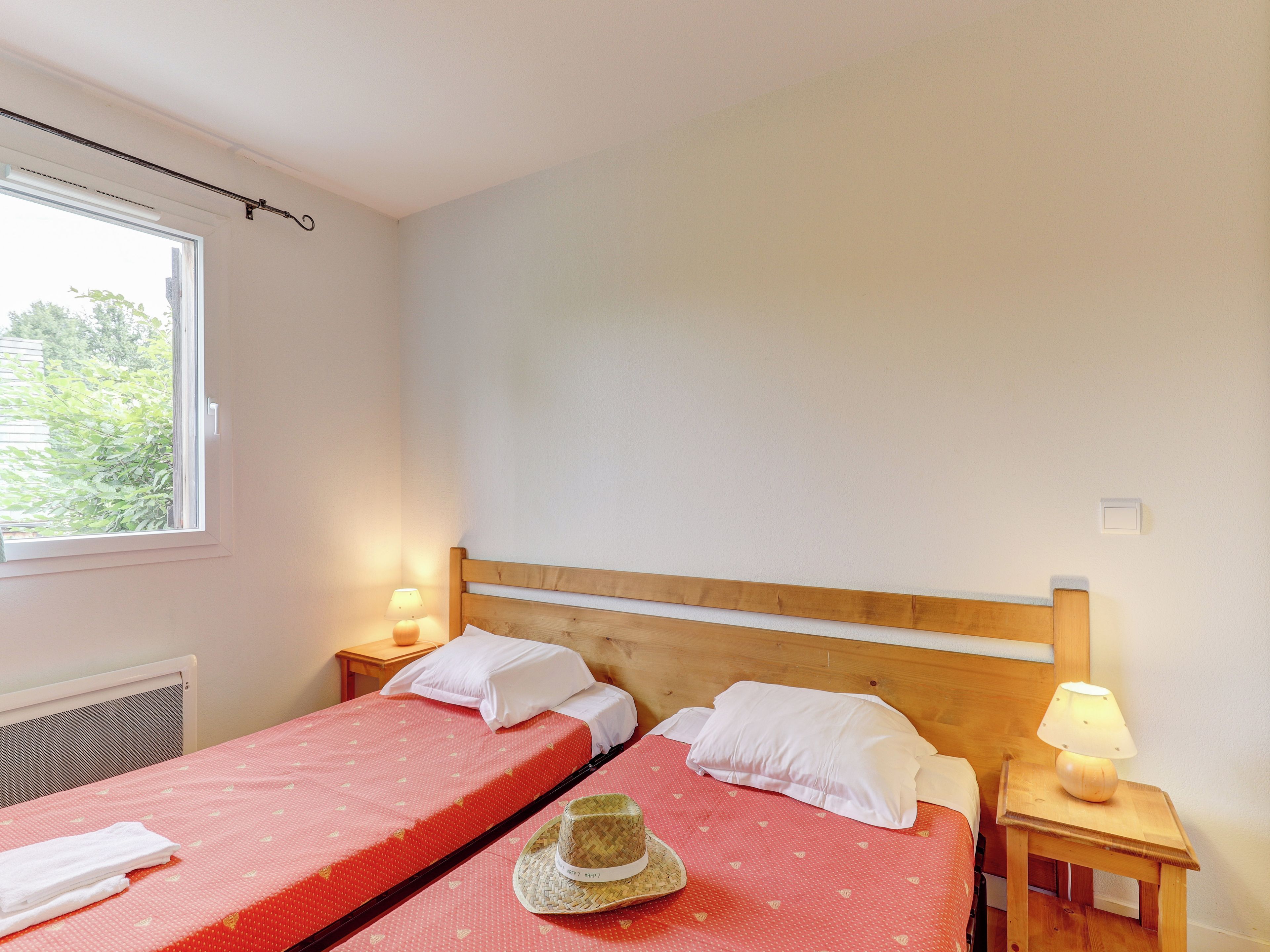 A bedroom with two beds, a window, and a nightstand with a lamp.