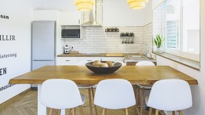 Een moderne keuken met witte kasten, een houten eettafel en twee hanglampen.